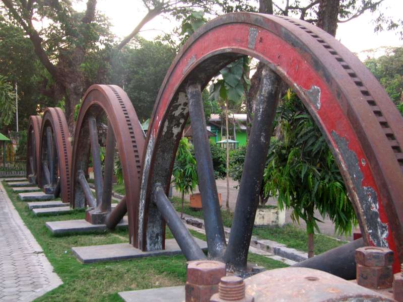 Tasikmadu: Schwungräder der ehemaligen Mühlenmaschinen als Exponate im Freien